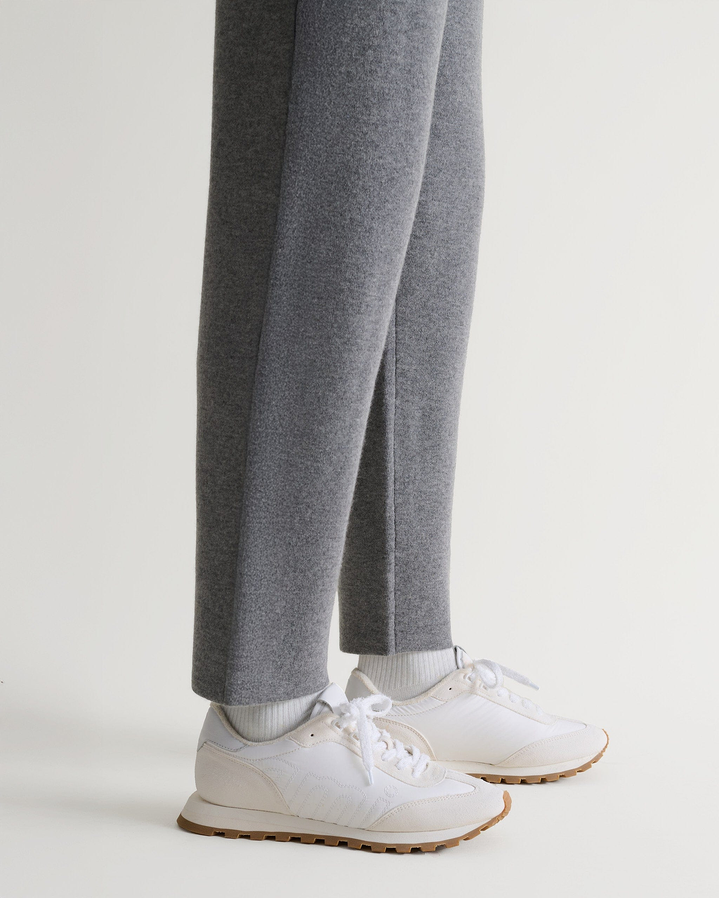 Bottom side view of Rise & Fall's grey cashmere merino double-faced joggers with white trainers. 