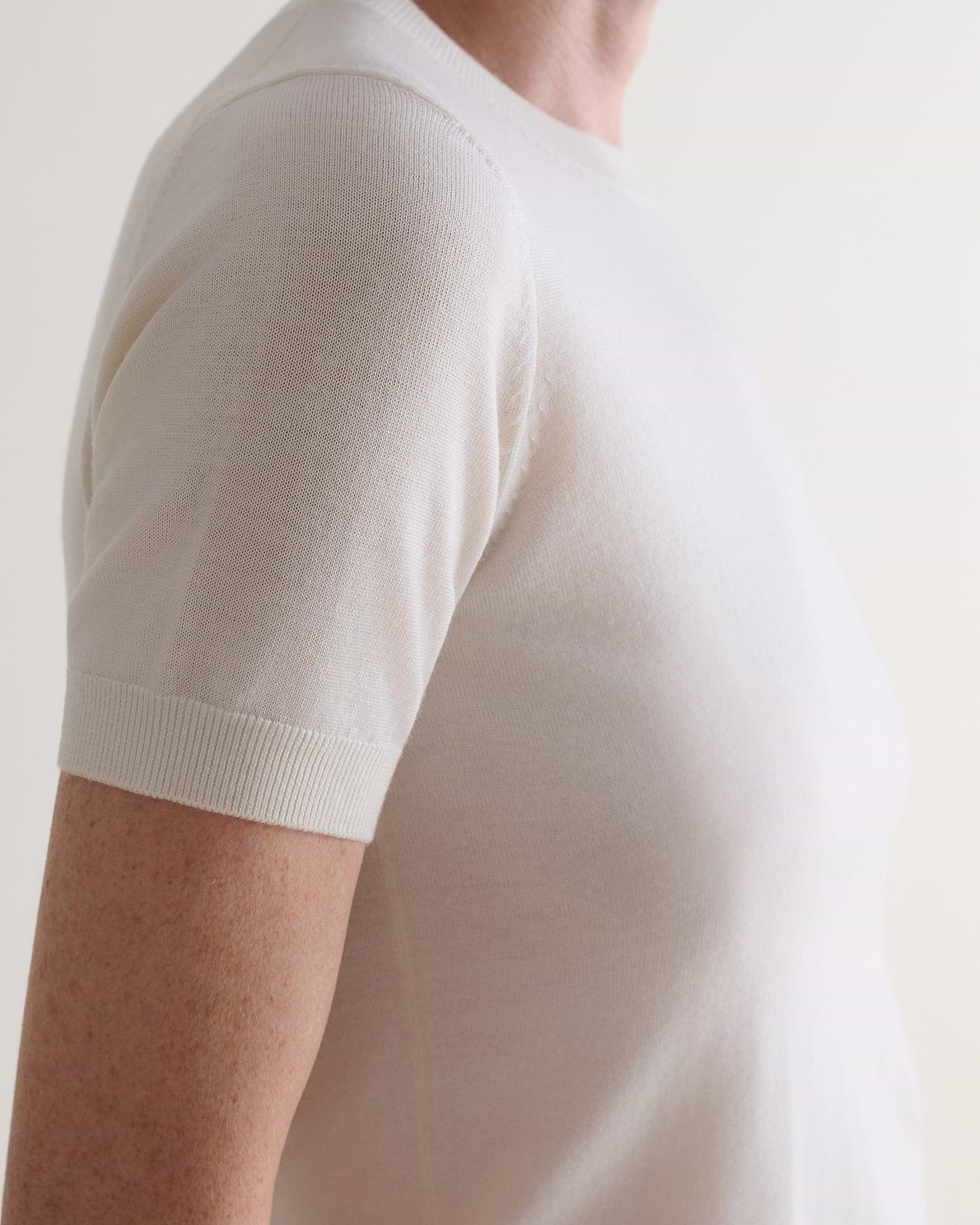 Close up side view of woman wearing Rise & Fall's cream superfine merino wool knitted t-shirt.