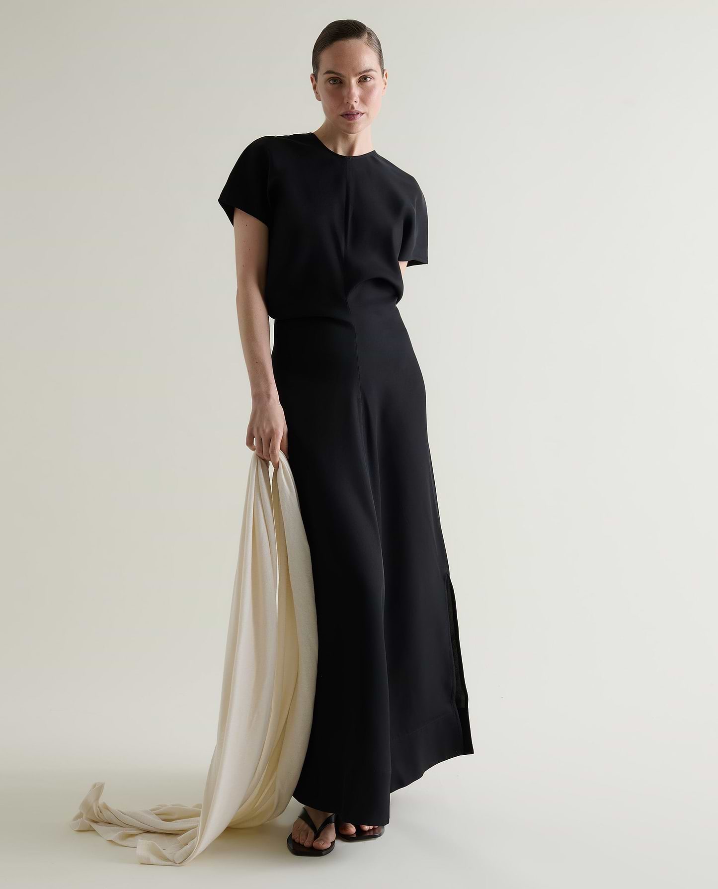 Woman wears black Naia maxi dress while holding a cream cashmere wrap.