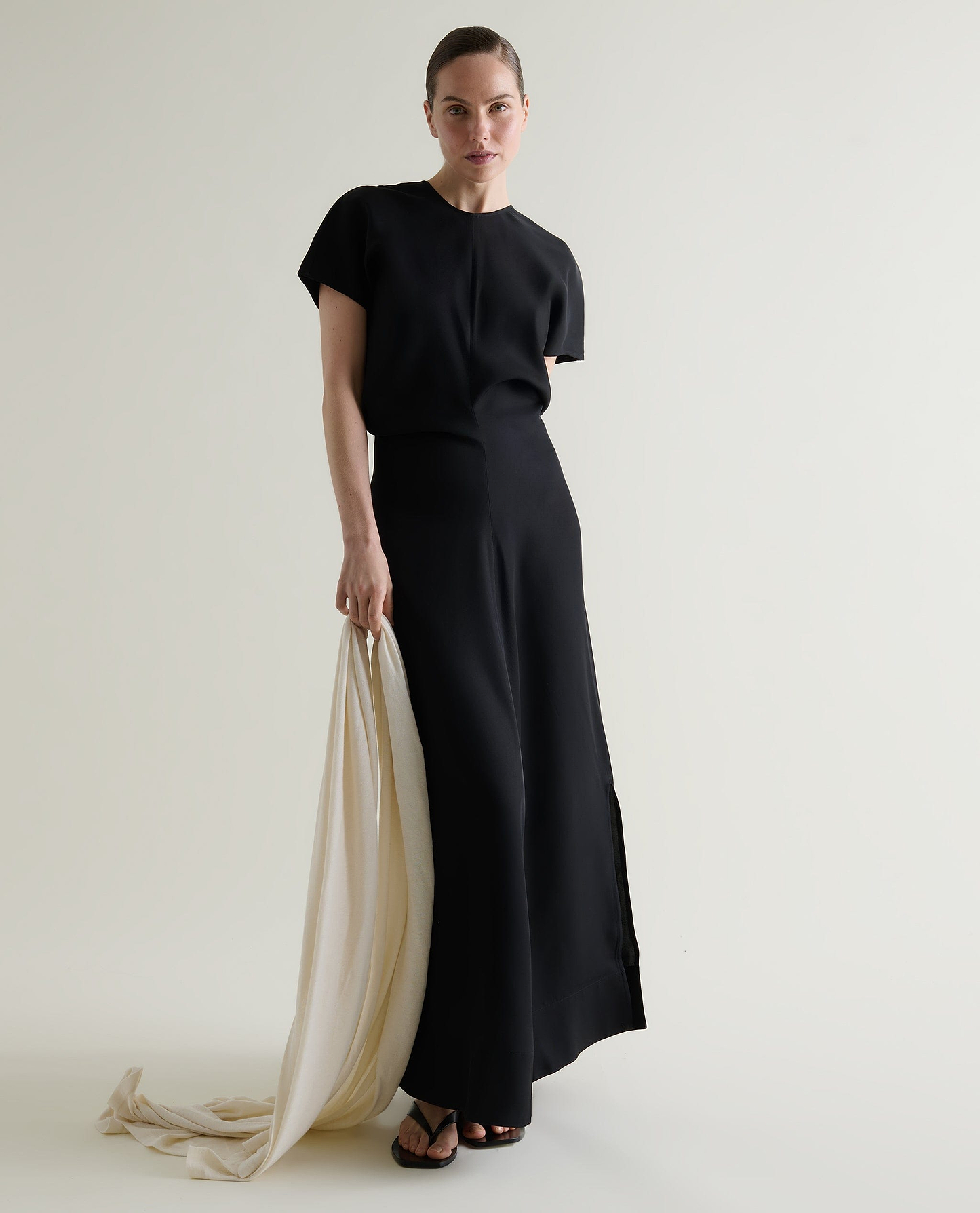Woman wears black Naia maxi dress while holding a cream cashmere wrap.