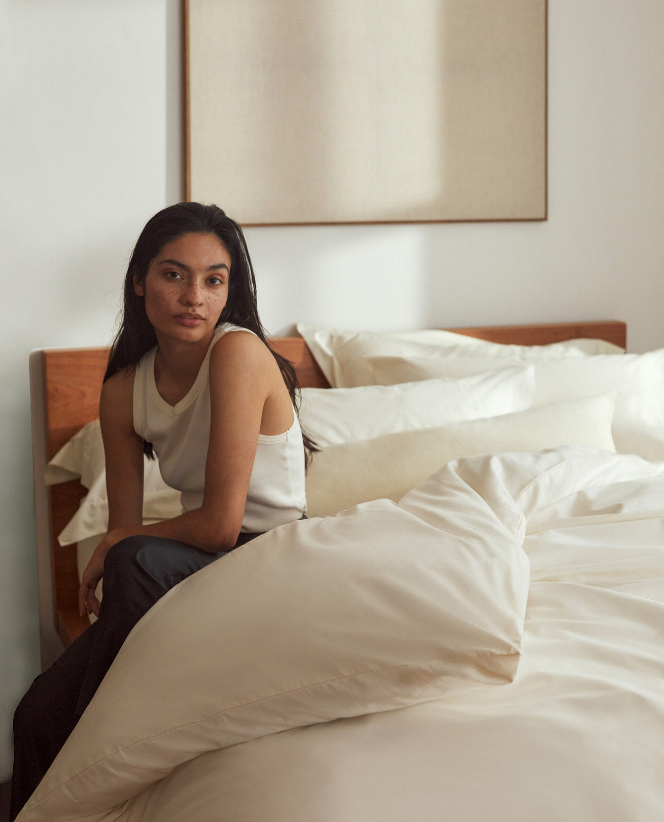 Woman sits on cotton bed linen.