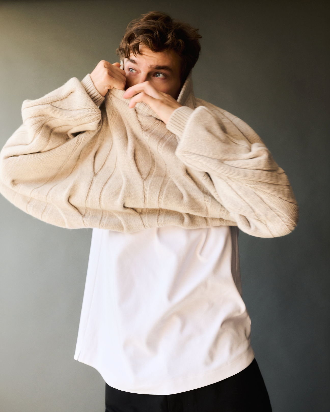 Man putting on Rise & Fall's Lambswool Cable Knit Jumper over a white T-shirt.
