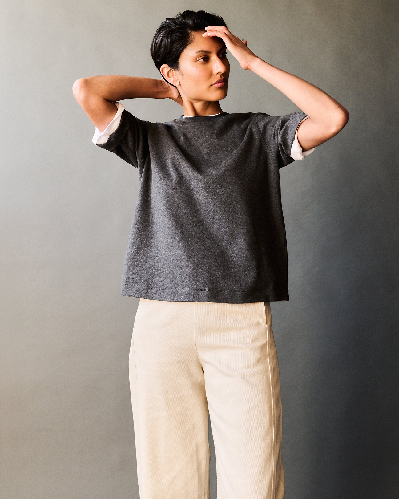 Woman wears a white and charcoal grey cre neck t-shirts with beige barrel leg trousers.