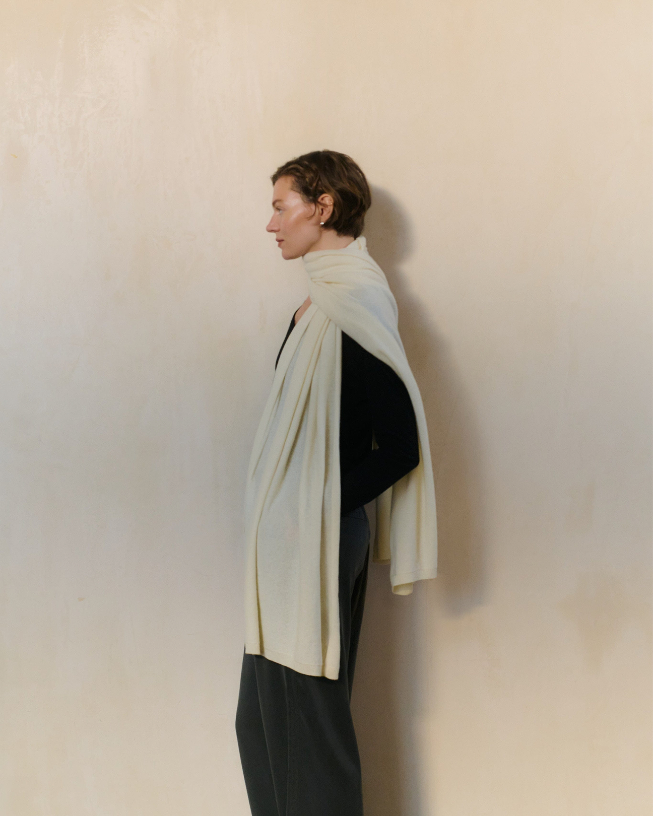 Woman Wraps Rise & Fall's Cream Cashmere Scarf Across Her Shoulders.