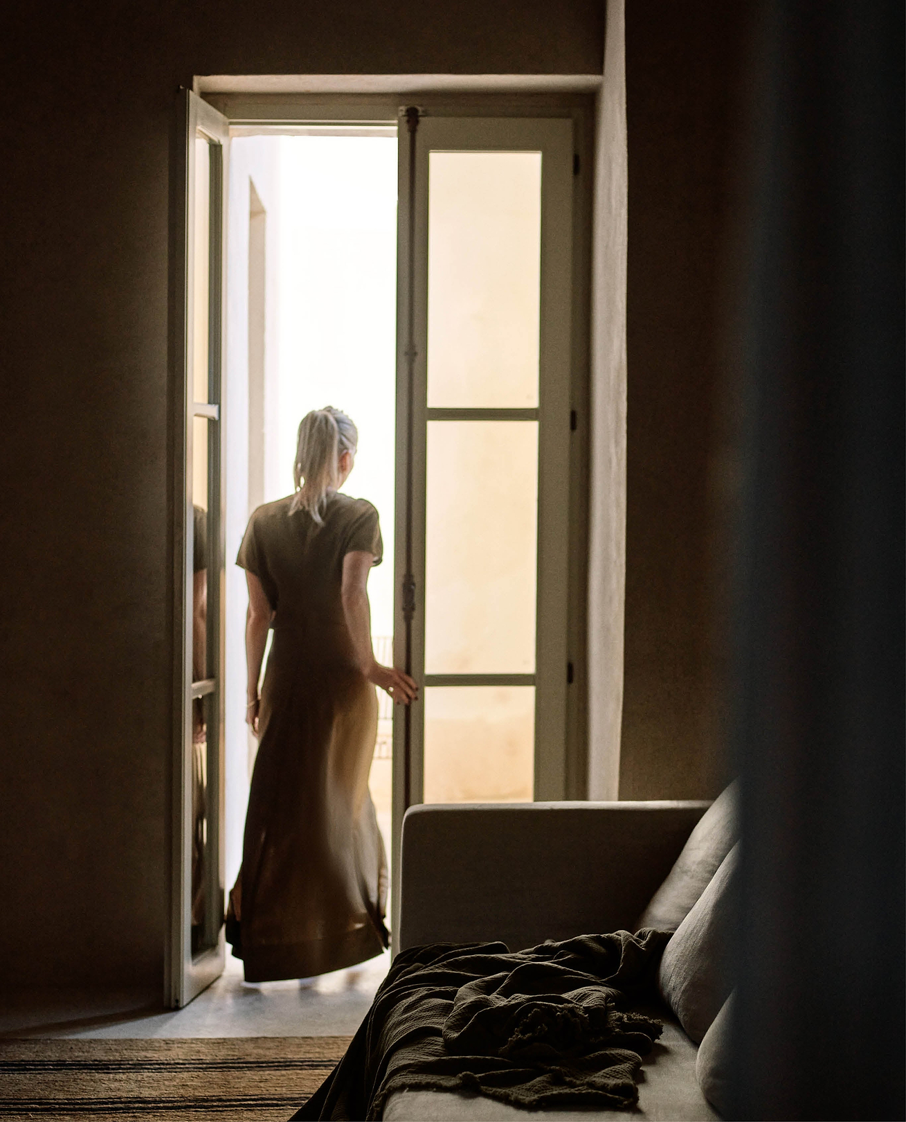 Woman walks through french doors into the sunlight.