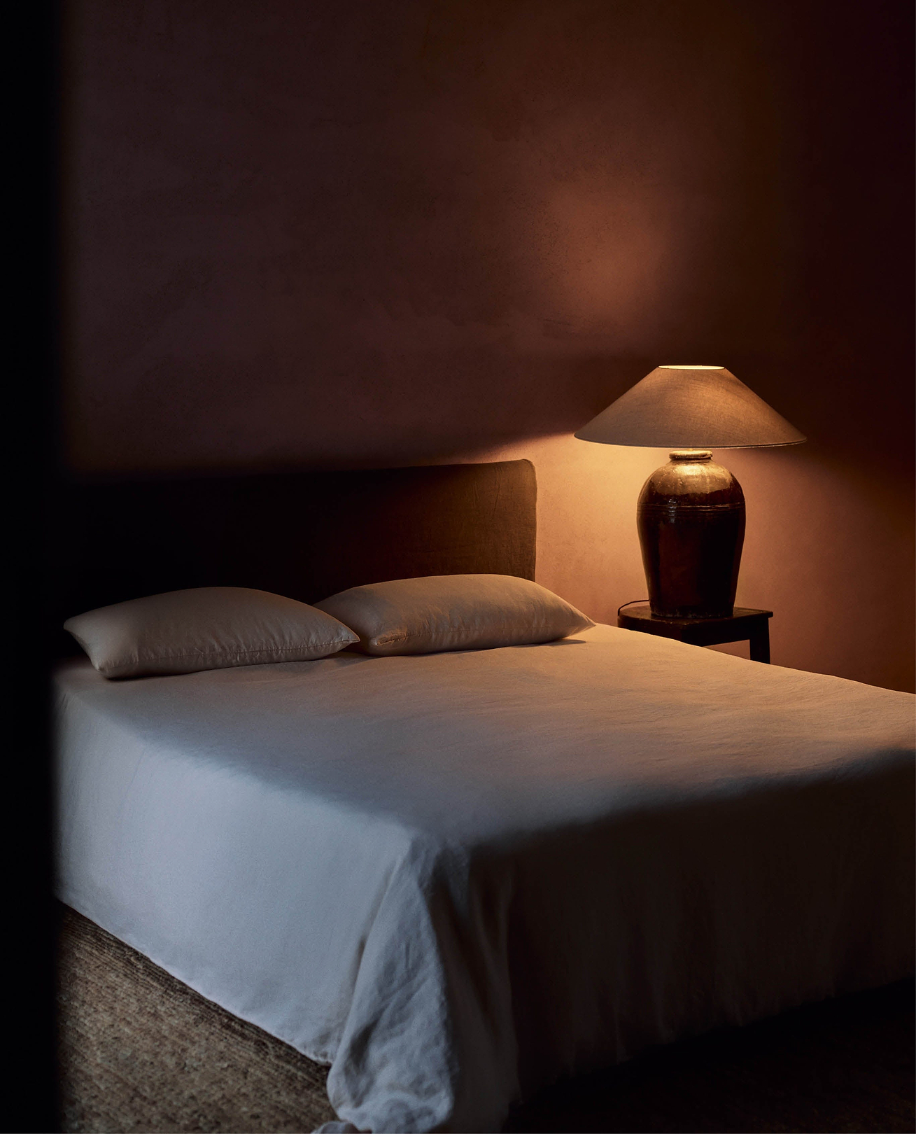Linen bedding with subtle lighting from bedside lamp.