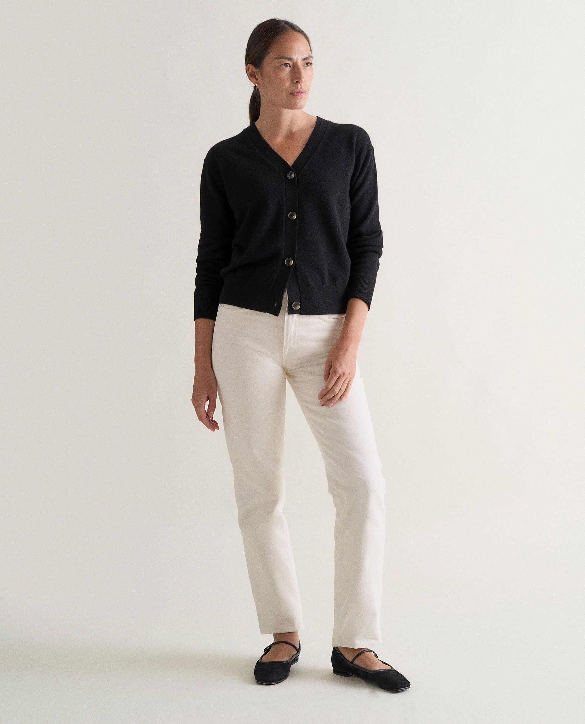 Image 1 of 3 showing woman wearing Rise & Fall's black fine cashmere v-neck cardigan with white jeans.