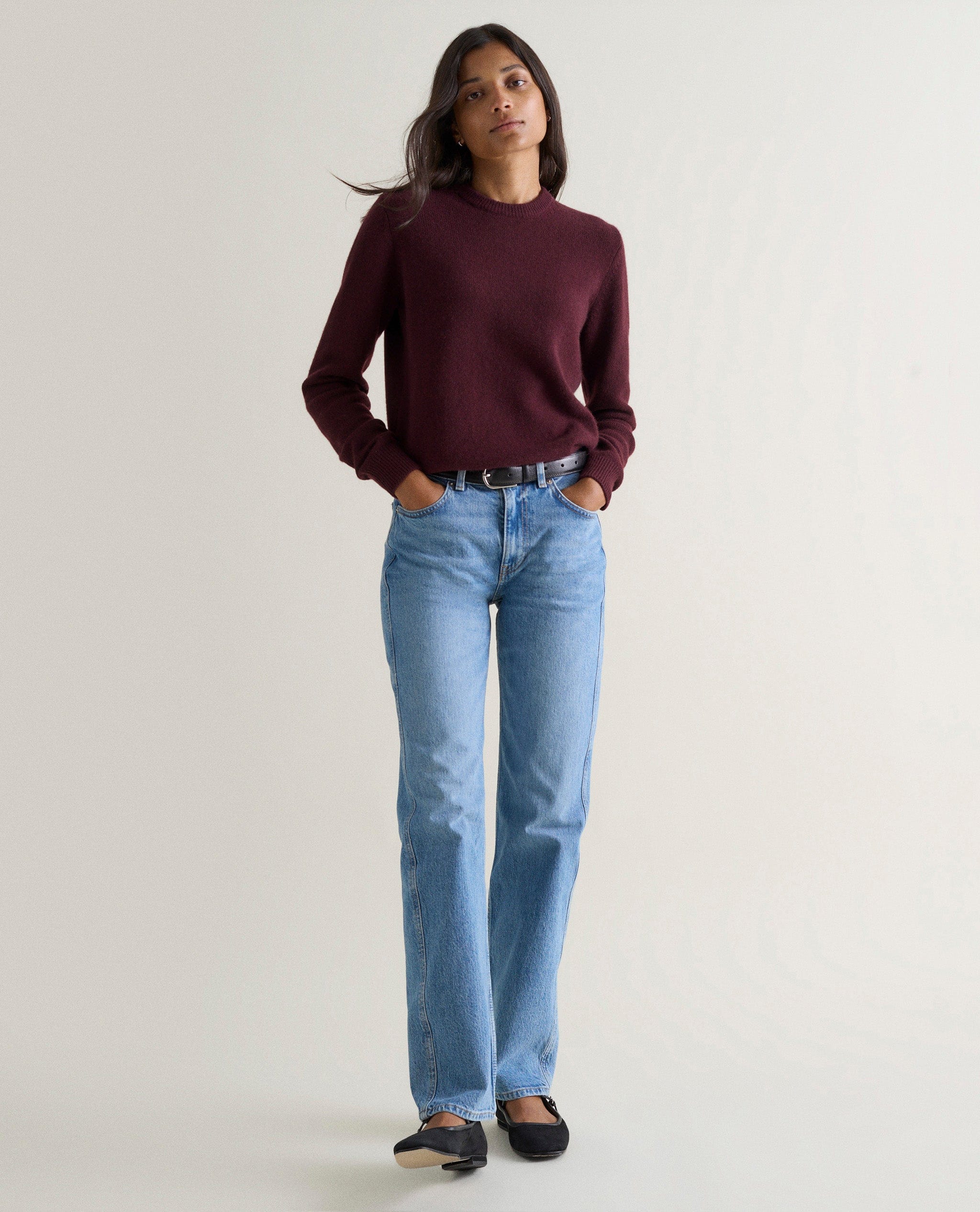 Image 1 of 3 showing woman wearing Rise & Fall's oxblood mid weight cashmere crew neck jumper with light blue jeans.