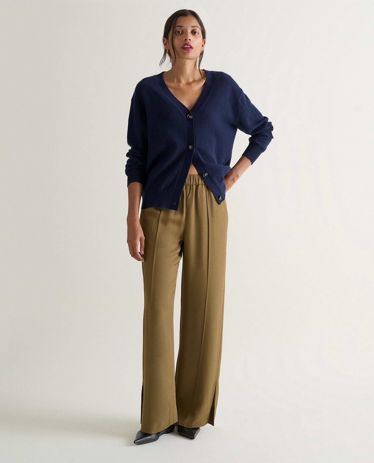 Image 1 of 4 showing woman wearing Rise & Fall's navy fine cashmere v-neck cardigan with olive trousers.