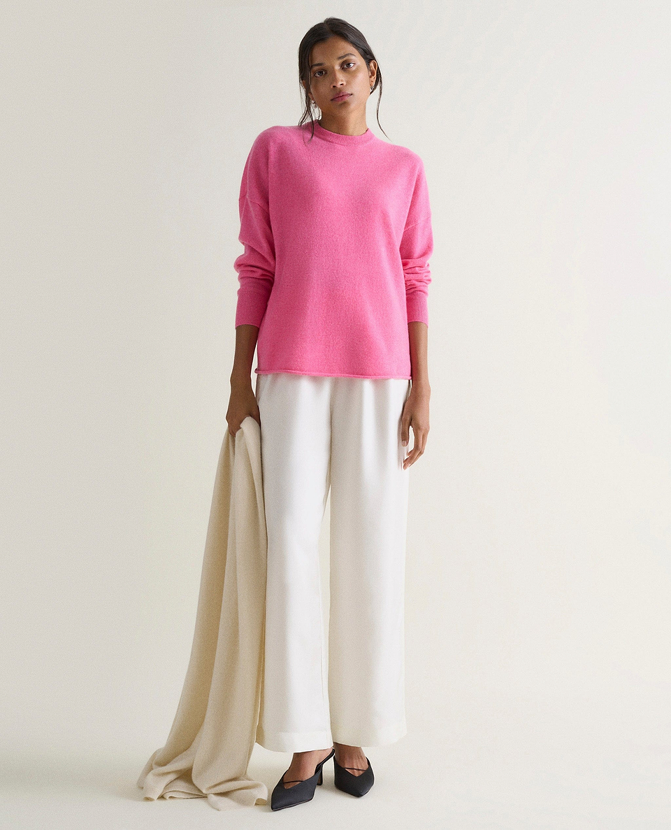 Image 1 of 4 showing woman wearing Rise & Fall's pink fine cashmere sweatshirt with white silk trousers.