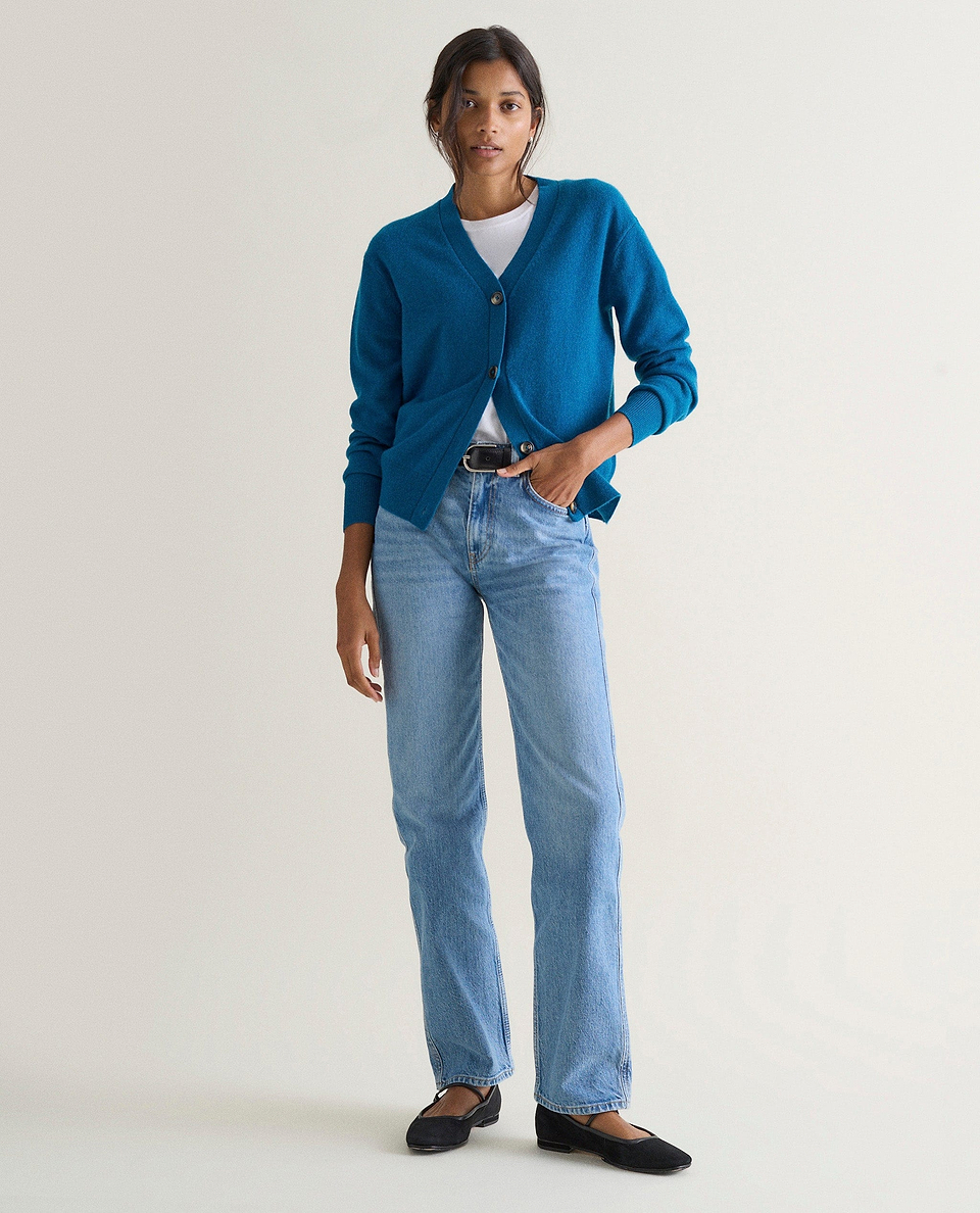 Image 1 of 5 showing a woman wearing Rise & Fall's viridian blue fine cashmere v-neck cardigan with a pair of jeans.