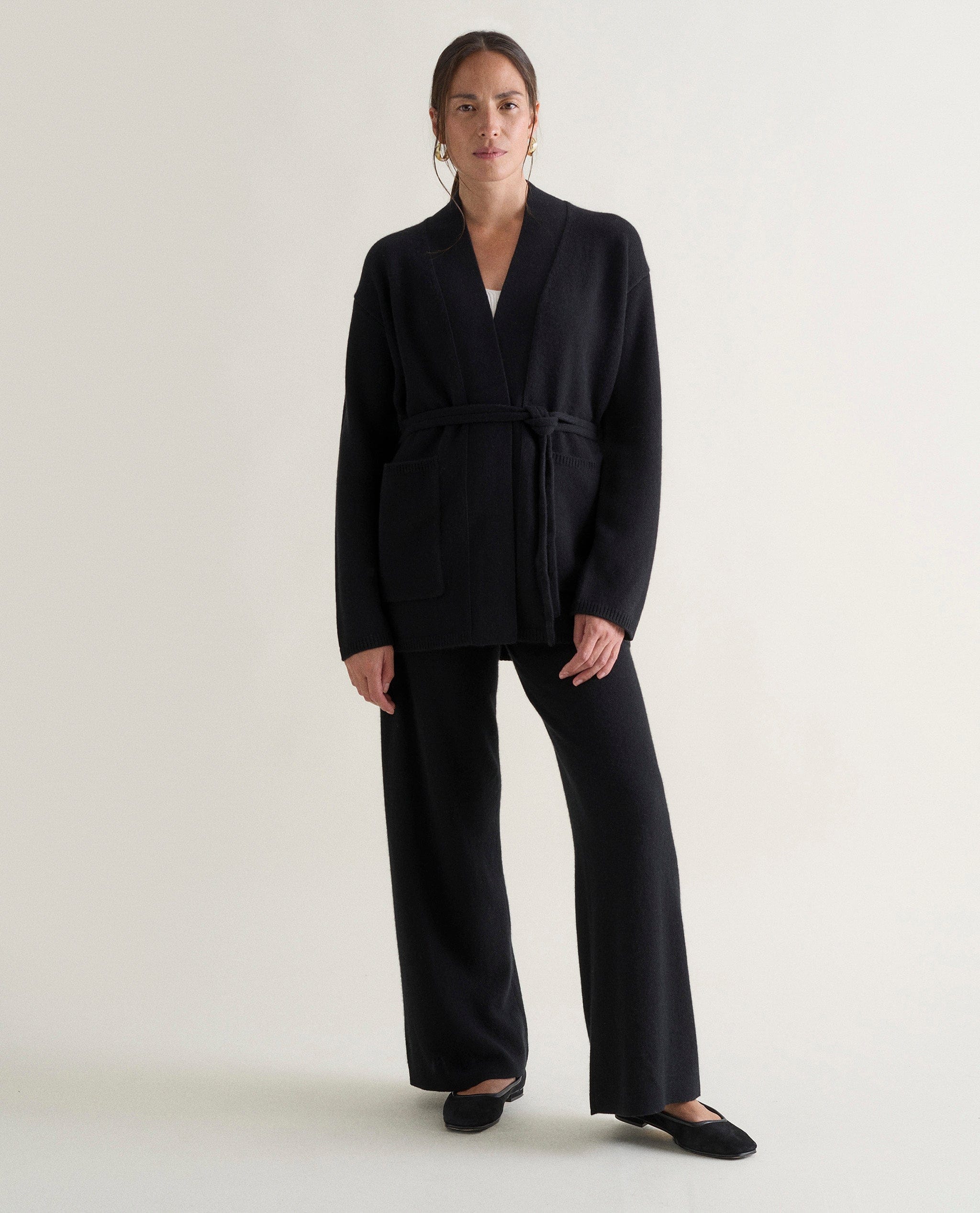 Image 1 of 5 showing woman wearing Rise & Fall's black cashmere merino belted cardigan with black trousers.