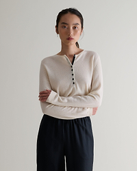 Image 1 of 5 showing a woman wearing Rise & Fall's buttermilk cashmere merino henley jumper with black silk trousers. 