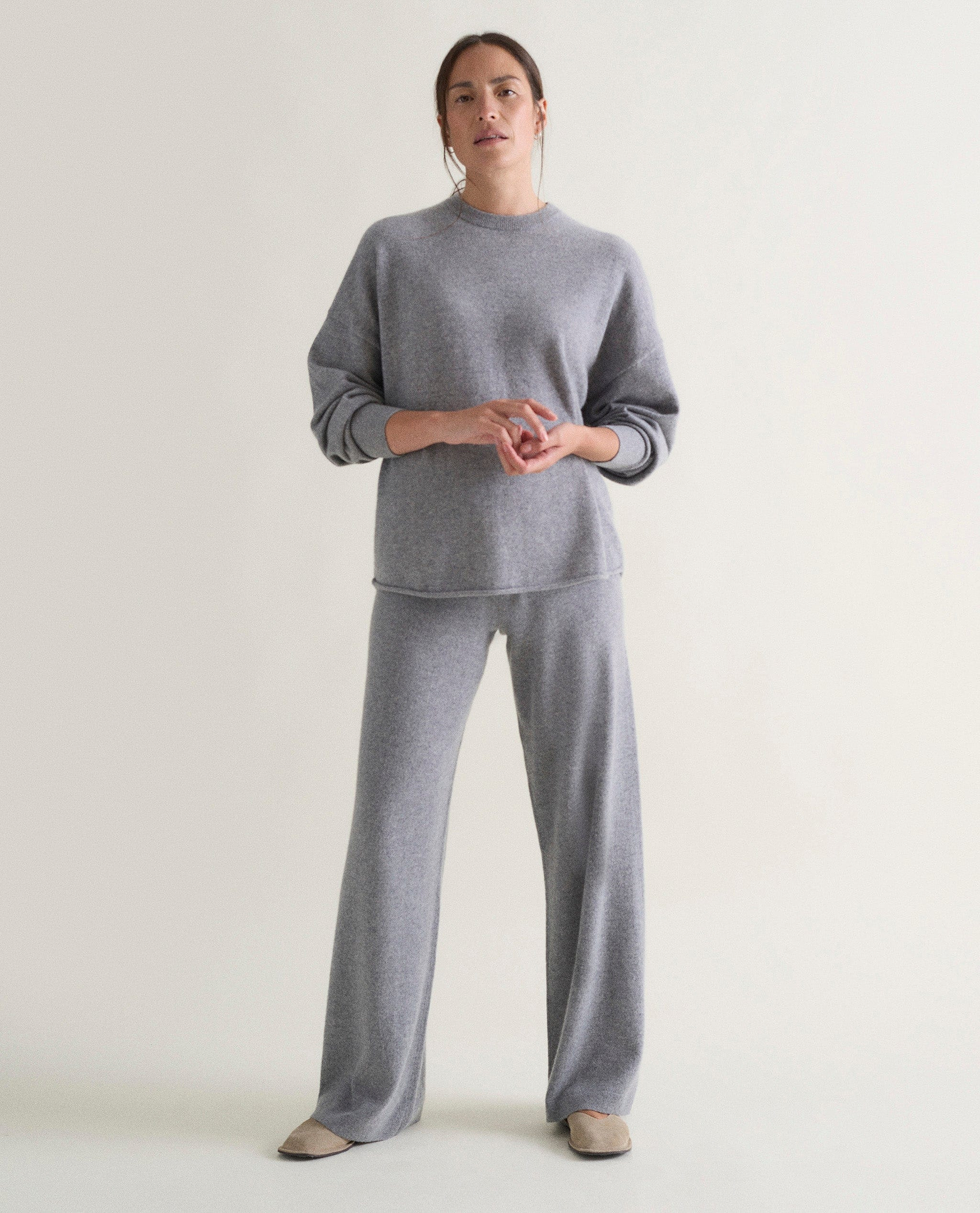 Image 1 of 5 showing woman wearing Rise & Fall's grey fine cashmere sweatshirt with matching cashmere trousers.