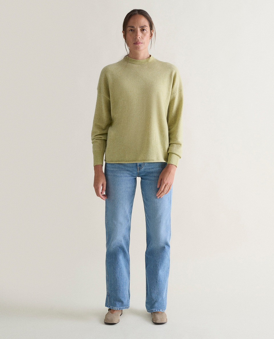 Image 1 of 5 showing woman wearing Rise & Fall's lichen green fine cashmere sweatshirt with pale blue jeans.