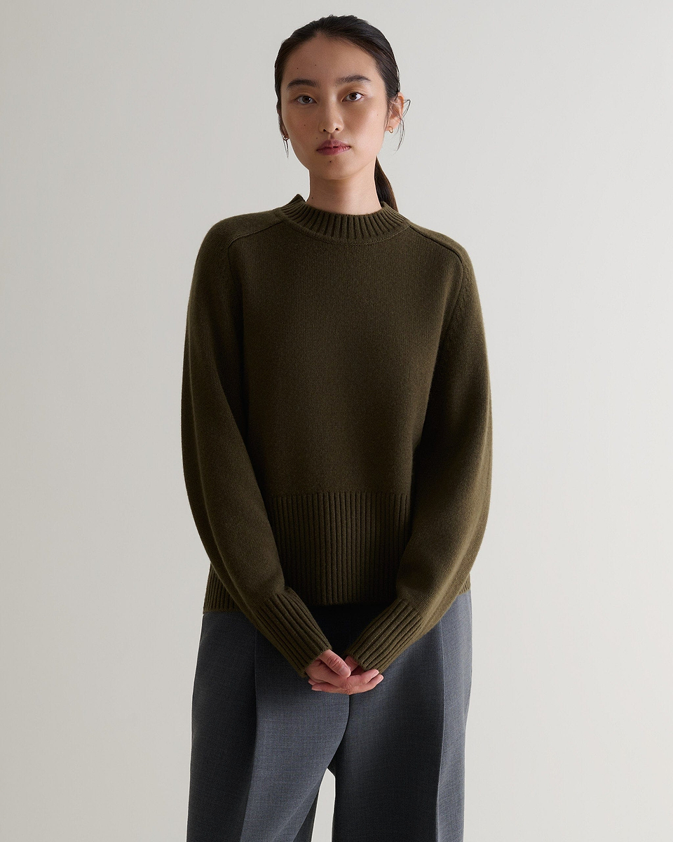 Image 1 of 5 showing woman wearing Rise & Fall's military green cashmere merino saddle sleeve crew neck jumper with grey trousers. 