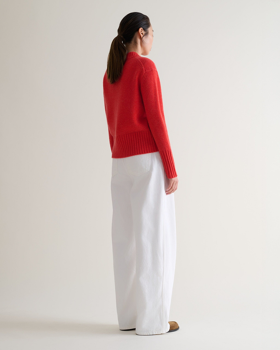 Image 1 of 6 showing back of woman wearing Rise & Fall poppy red cashmere merino saddle sleeve crew neck jumper, with white wide leg jeans.