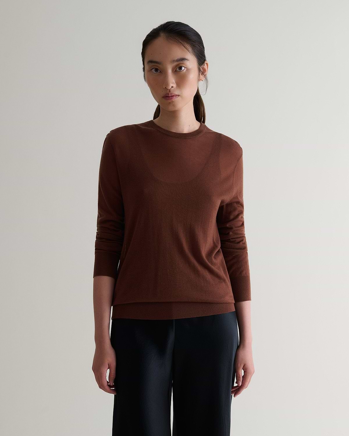 Image 1 of 6 showing woman wearing Rise & Fall's brown tencel cashmere double layered crew neck jumper with black trousers.