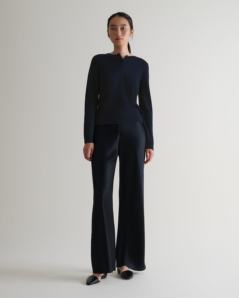 Image 1 of 6 showing a woman wearing Rise & Fall's indigo cashmere merino henley jumper with black silk trousers. 