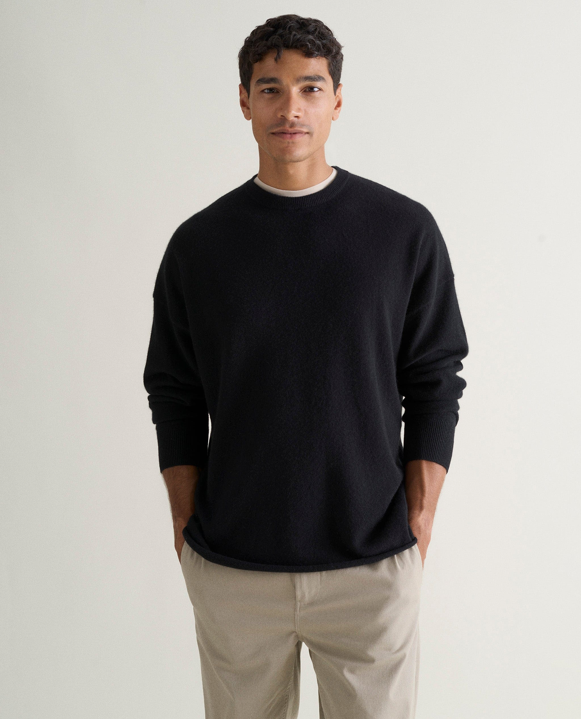 Image 3 of 5 showing man wearing Rise & Fall's black finest cashmere sweatshirt over white T-shirt and stone-coloured trousers.
