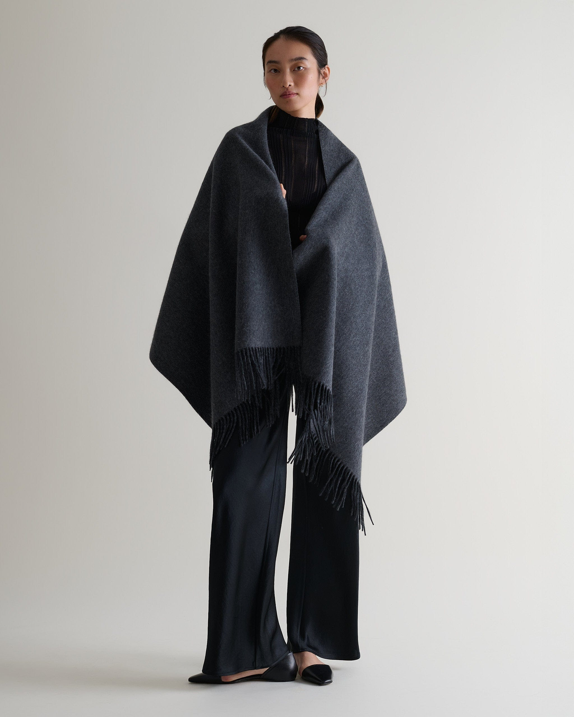 Image 3 of 5 showing woman wearing Rise & Fall's finest cashmere double faced wrap over shoulders, colour: charcoal and black.