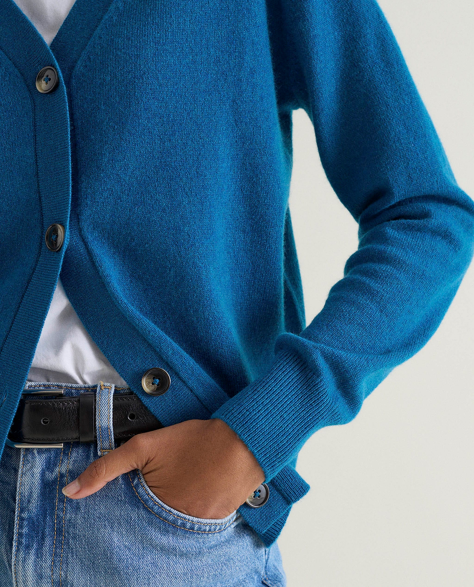 Image 3 of 5 showing a close up of woman wearing Rise & Fall's viridian blue fine cashmere v-neck cardigan with white top, pair of jeans and a black belt.