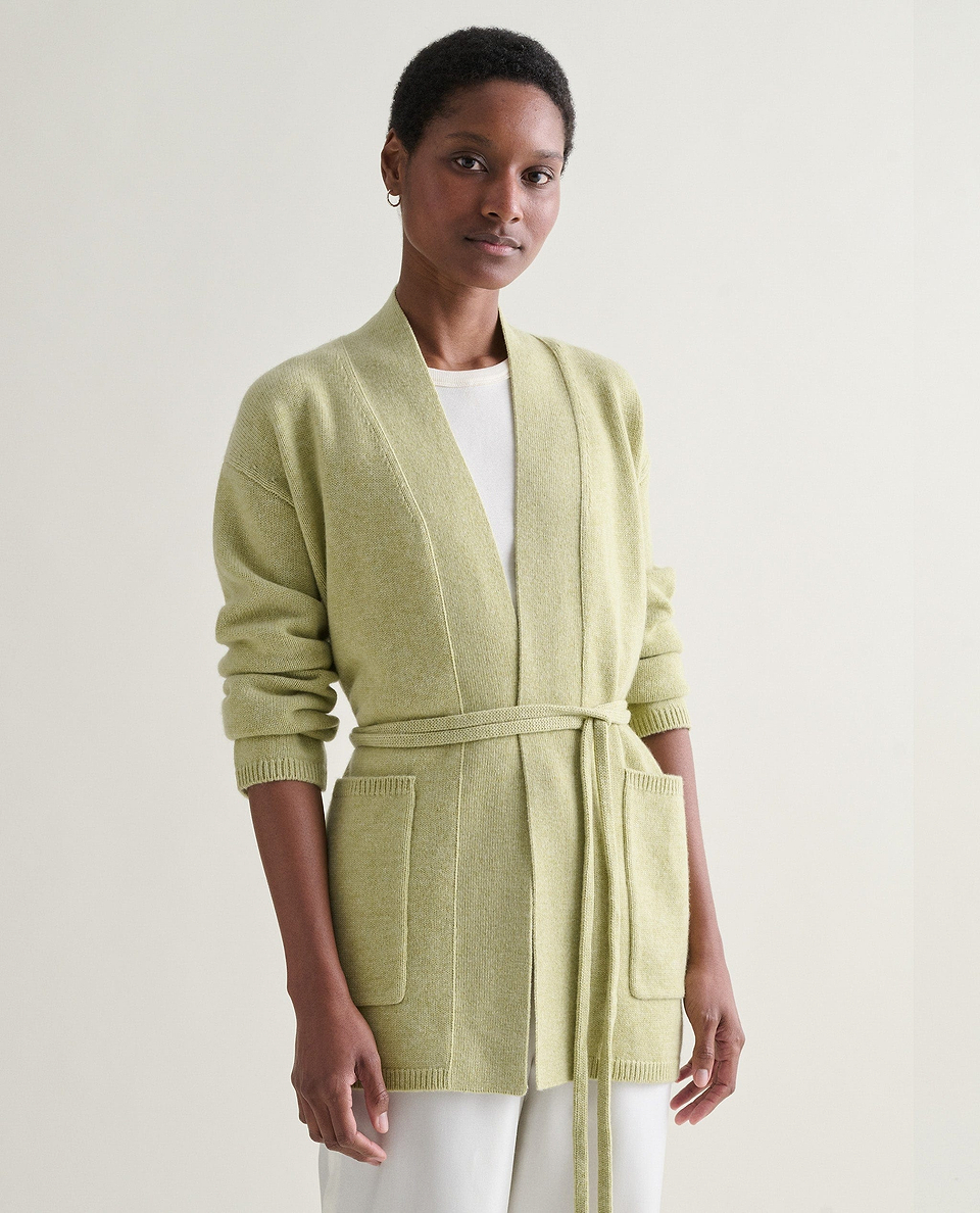 Image 3 of 5 showing woman wearing Rise & Fall's lichen green cashmere merino belted cardigan with white t-shirt and trousers.