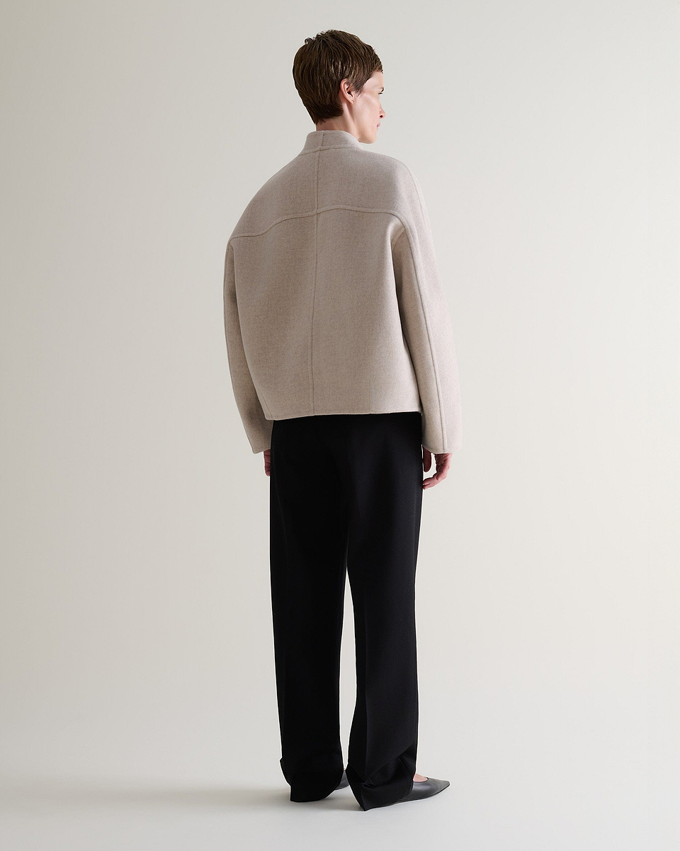 Image 3 of 9 showing back view of woman wearing Rise & Fall's twine cashmere wool double faced scarf jacket with black trousers.