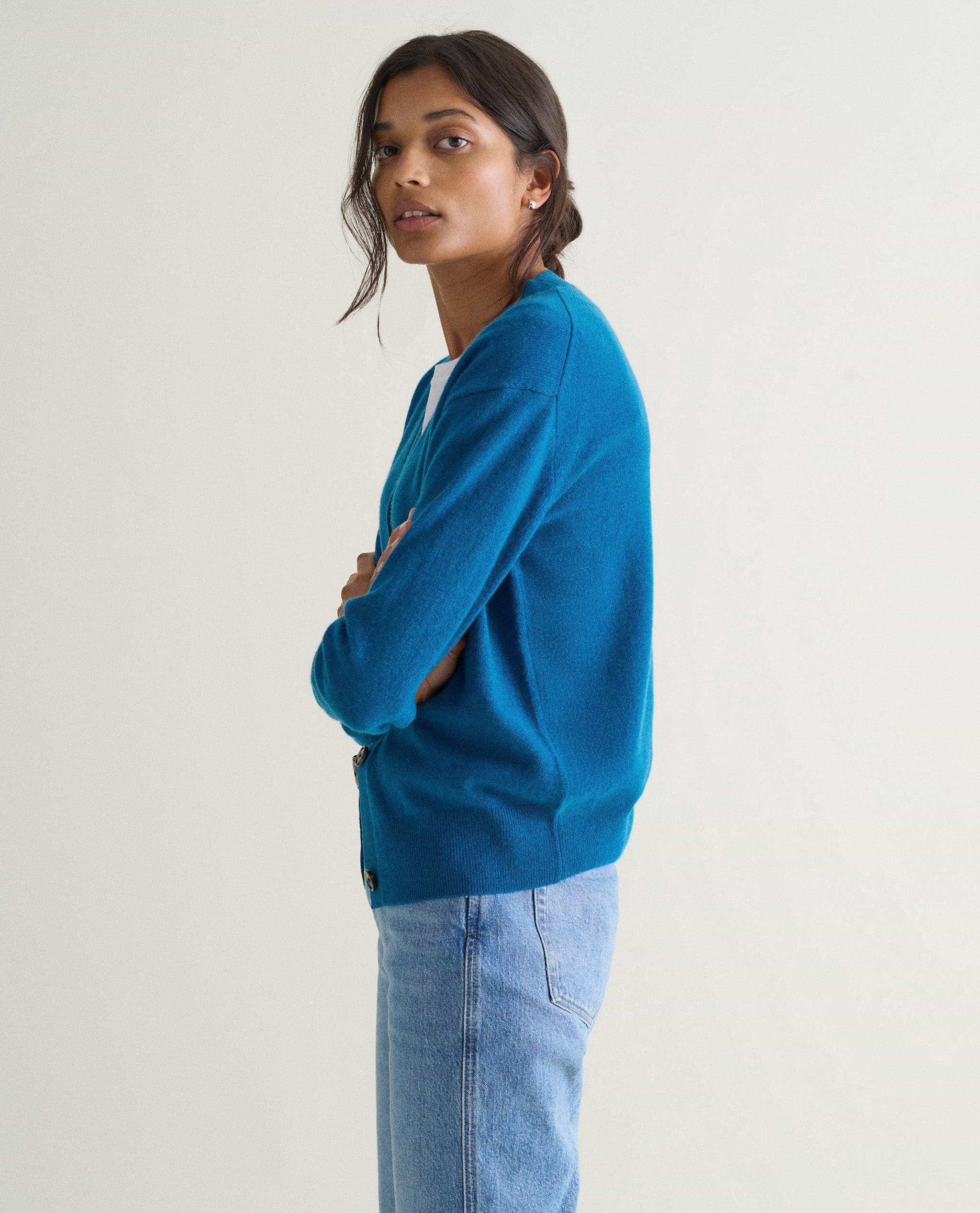 Image 4 of 5 showing side view of a woman wearing Rise & Fall's viridian blue fine cashmere v-neck cardigan with a pair of jeans.
