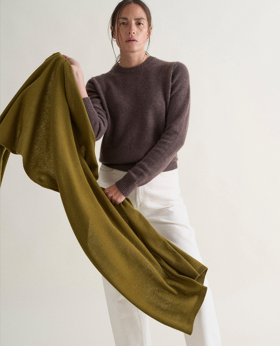 Image 4 of 5 showing woman wearing Rise & Fall's brown mid-weight cashmere crew neck jumper with white jeans while holding an olive green cashmere wrap