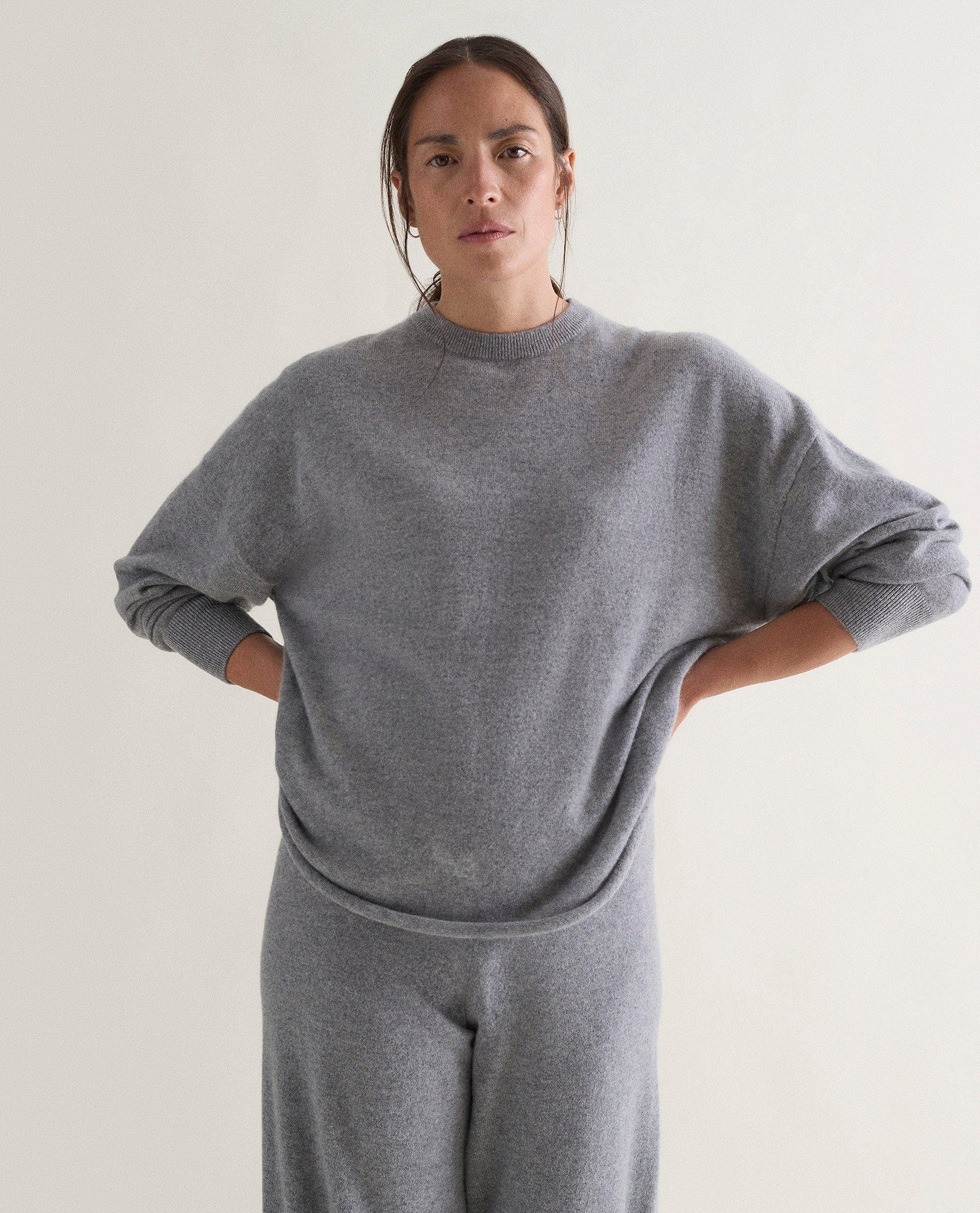 Image 4 of 5 showing woman wearing Rise & Fall's grey fine cashmere sweatshirt with matching cashmere trousers.