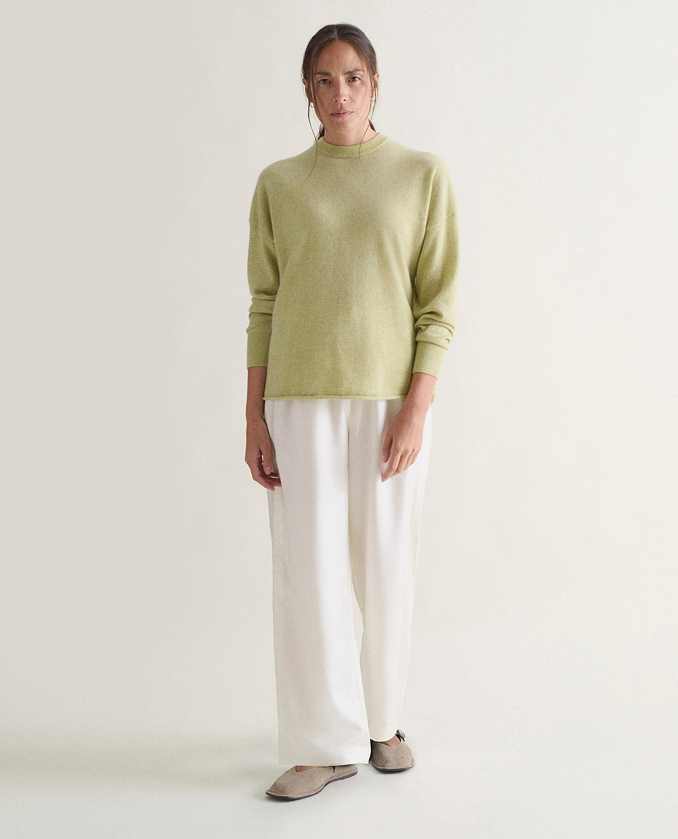 Image 4 of 5 showing woman wearing Rise & Fall's lichen green fine cashmere sweatshirt with white trousers.