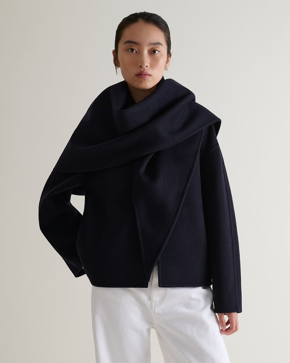 Image 4 of 7 showing woman wearing Rise & Fall's navy cashmere wool double faced scarf jacket with white jeans.