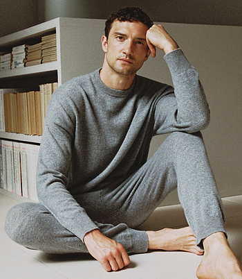 Image 5 of 5 showing man sat on floor wearing Rise & Fall's finest cashmere sweatshirt in grey with matching joggers.
