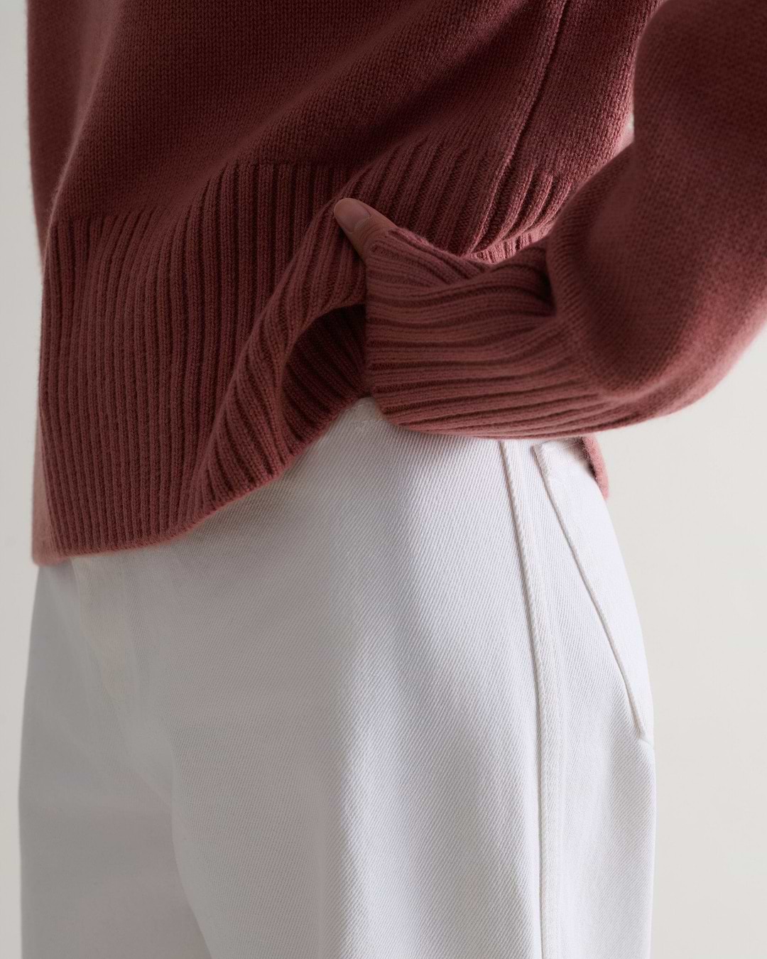 Image 5 of 5 showing a close up of Rise & Fall's pink clay cashmere merino saddle sleeve crew neck jumper with white jeans.