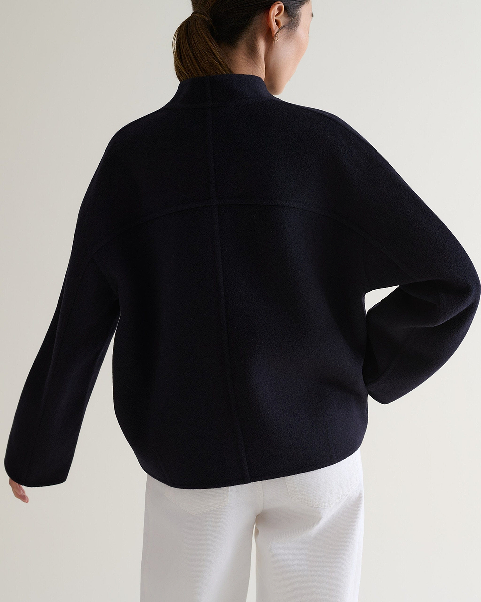 Image 5 of 7 showing back view of woman wearing Rise & Fall's navy cashmere wool double faced scarf jacket with white jeans.