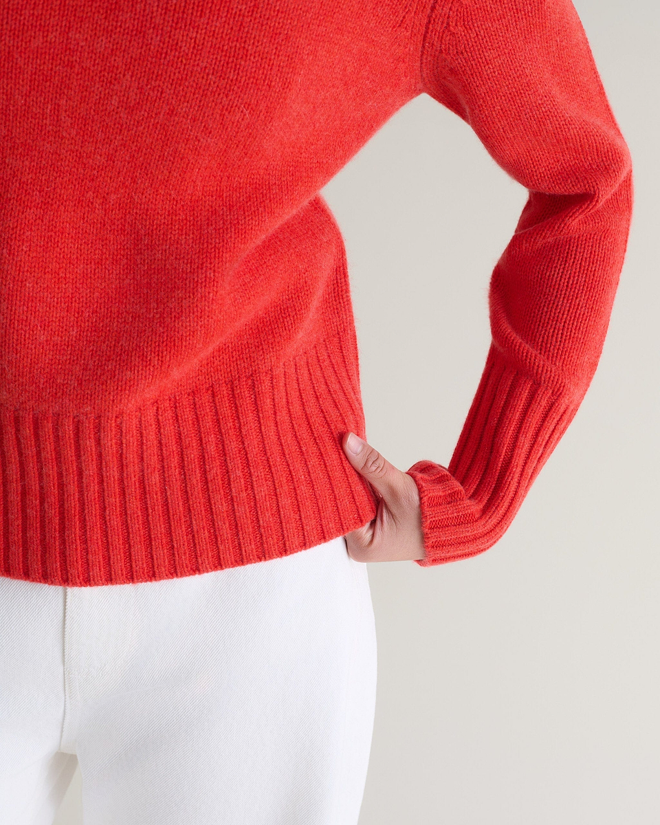 Image 6 of 6 showing close up of Rise & Fall's poppy red cashmere merino saddle sleeve crew neck jumper with white jeans.
