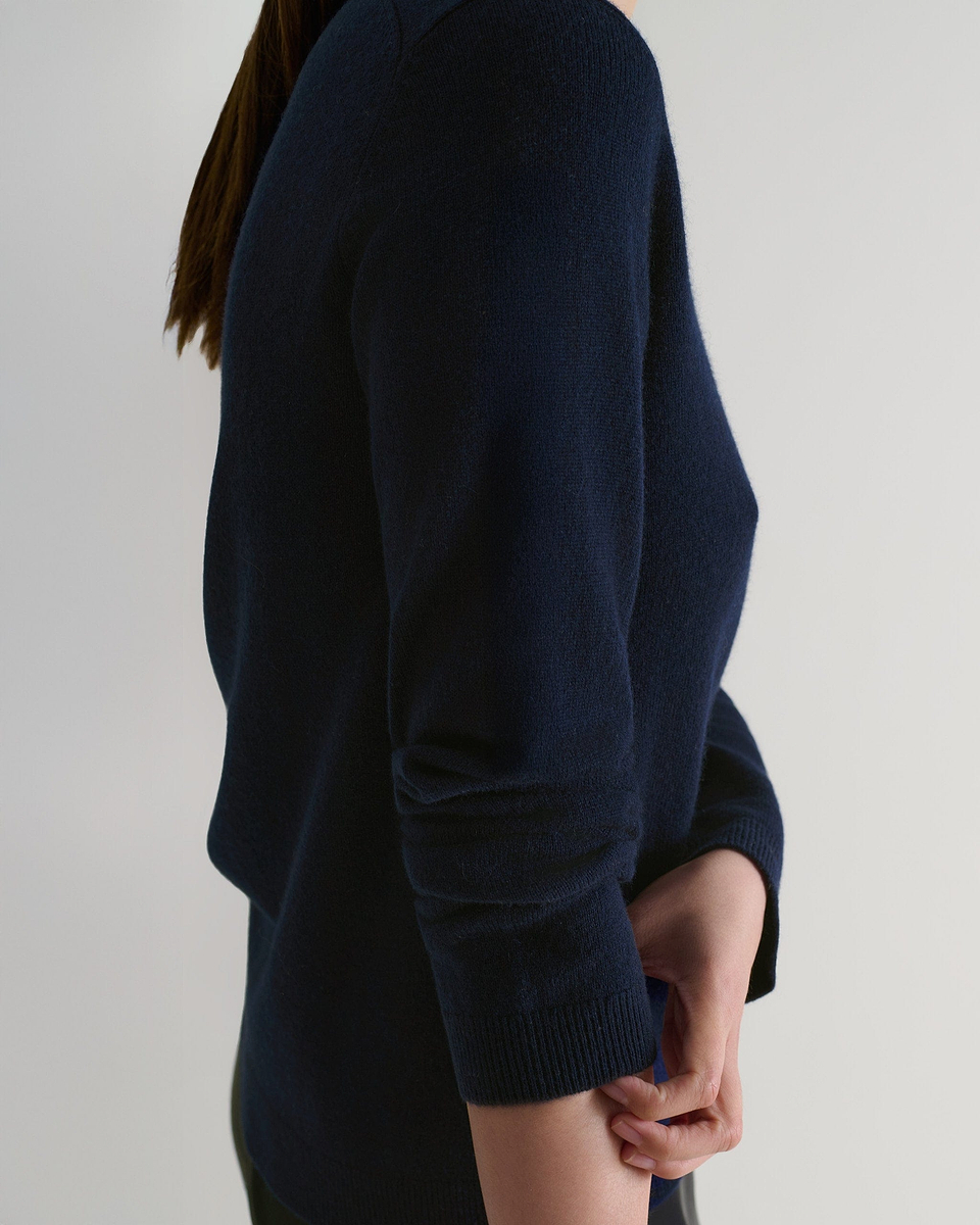 Image 6 of 6 showing side view of a woman wearing Rise & Fall's indigo cashmere merino henley jumper with black silk trousers. 