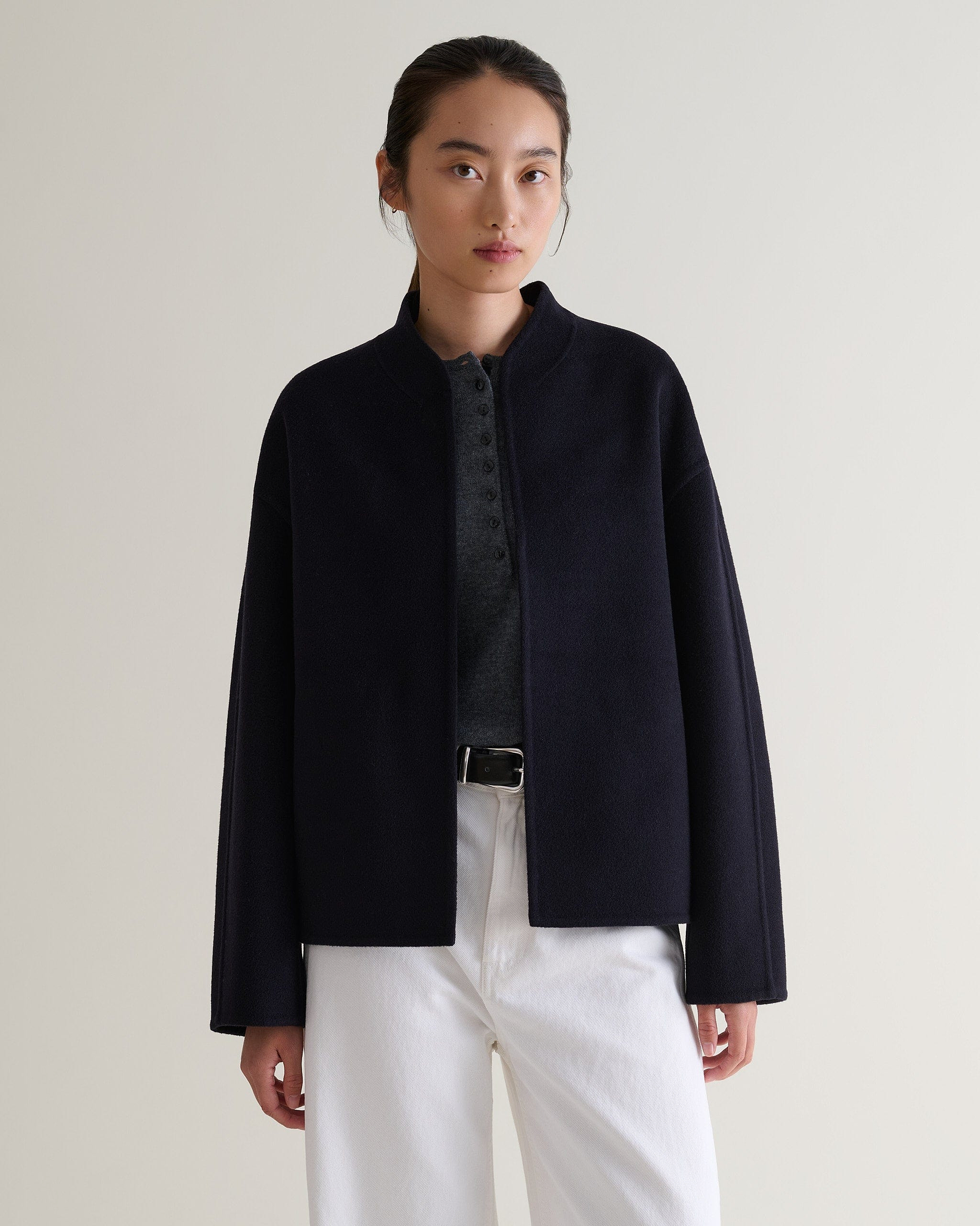 Image 6 of 7 showing woman wearing Rise & Fall's navy cashmere wool double faced jacket with white jeans and grey henley top.