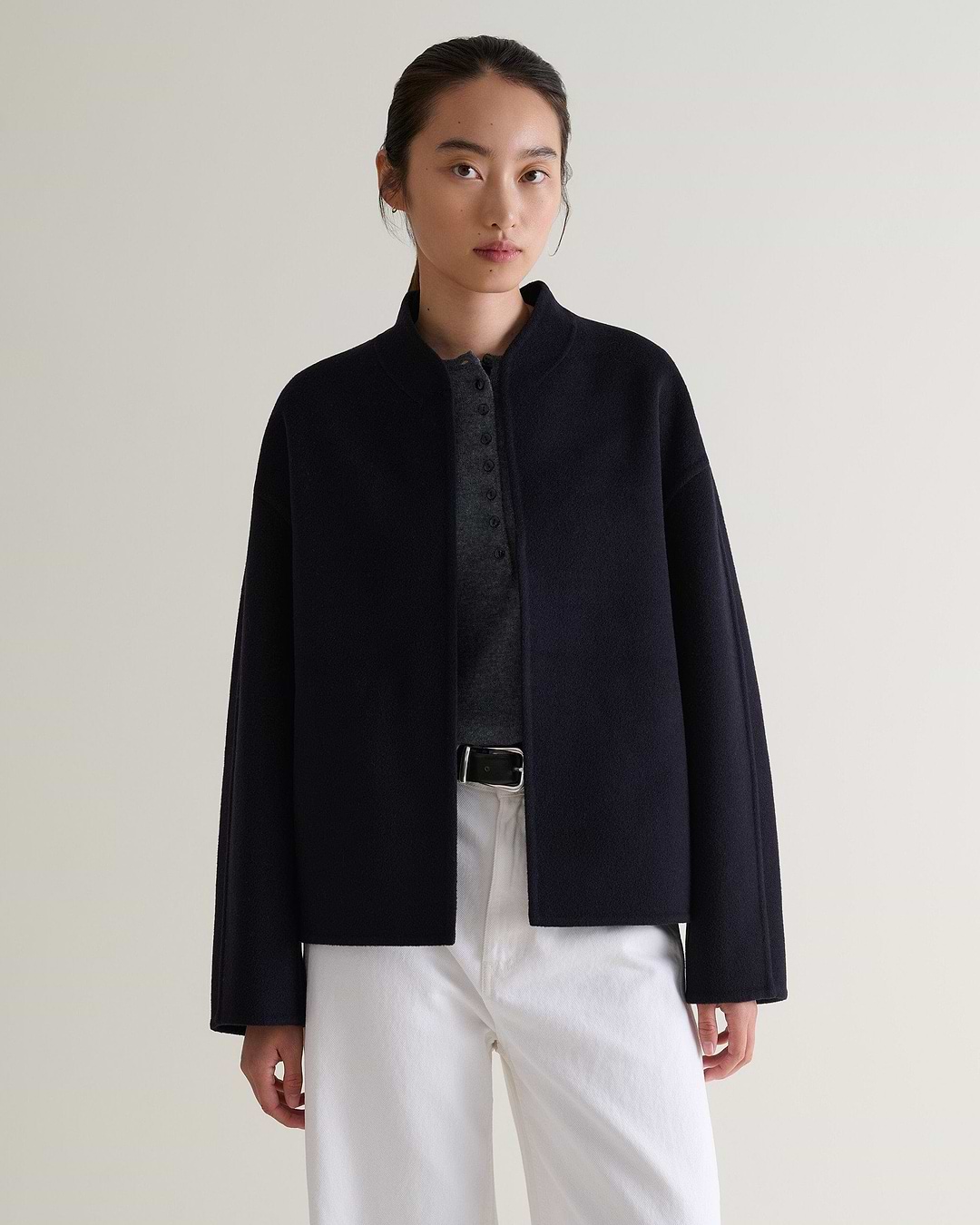 Image 6 of 7 showing woman wearing Rise & Fall's navy cashmere wool double faced jacket with white jeans and grey henley top.