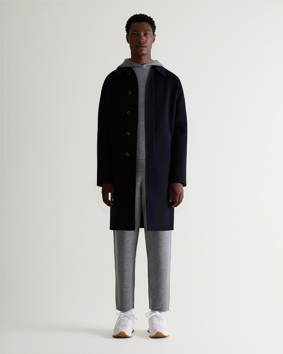 Full front view of man wearing Rise & Fall's grey cashmere merino double-faced hoodie and joggers with black wool coat.