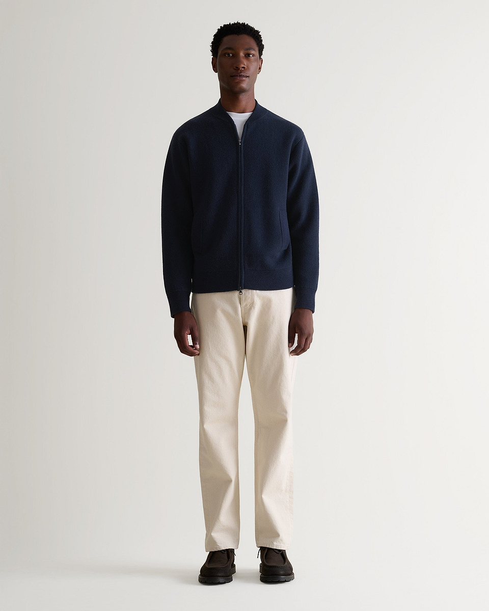 Man wearing Rise & Fall's navy cashmere merino double-faced knitted bomber jacket with cream jeans and white T-shirt.