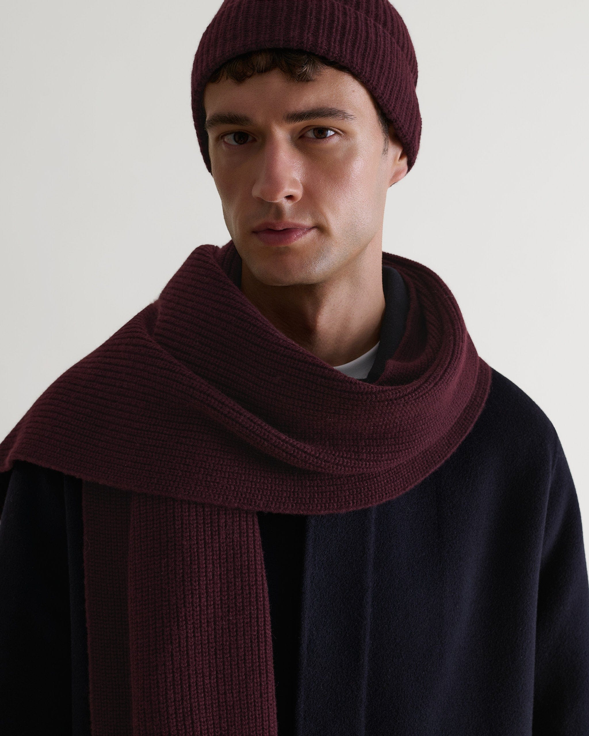 Close up of man wearing Rise & Fall's oxblood cashmere merino ribbed scarf with matching coloured beanie and navy wool coat