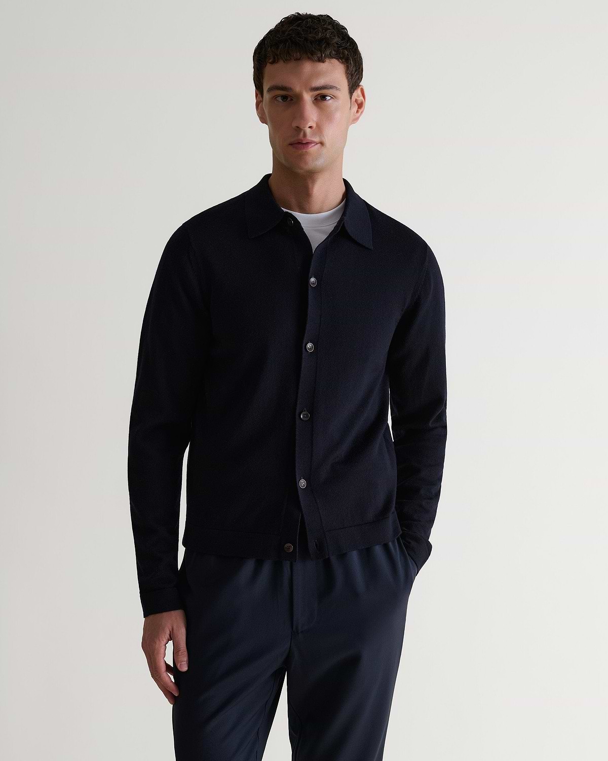 Front view of man wearing Rise & Fall's navy fine merino knit shirt. Worn with navy trousers and a white T-shirt.