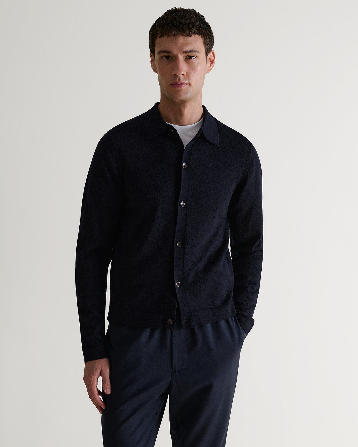 Front view of man wearing Rise & Fall's navy fine merino knit shirt. Worn with navy trousers and a white T-shirt.