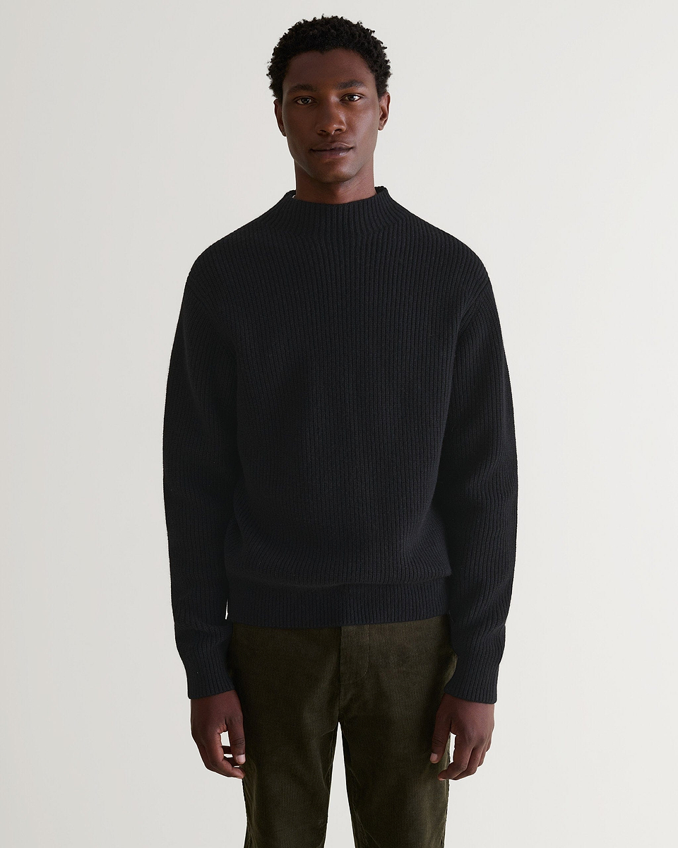 Front view of man wearing Rise & Fall's black cashmere merino stand neck ribbed sweater with dark green corduroy trousers.