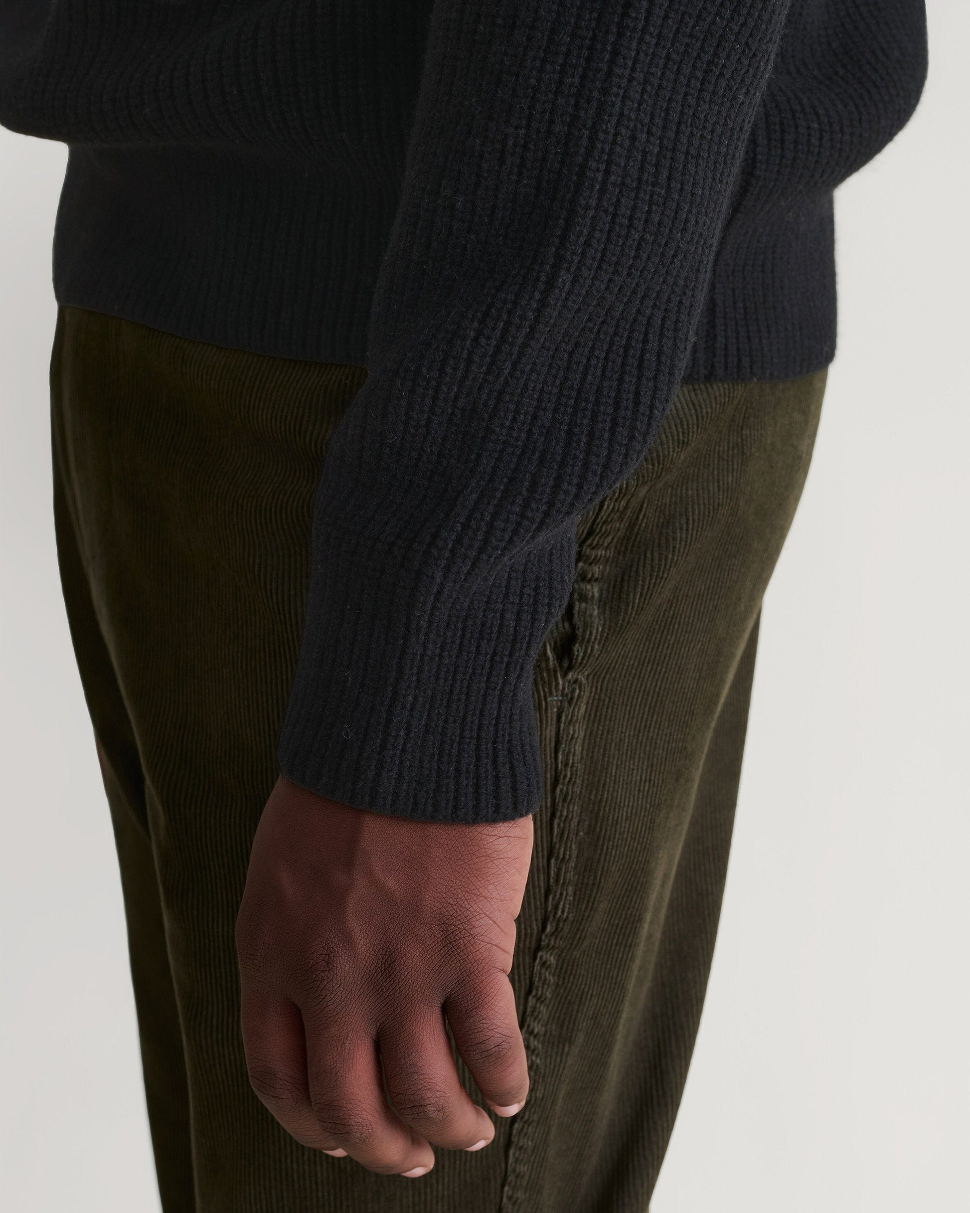 Side view of Rise & Fall's black cashmere merino stand neck jumper. Paired with dark green corduroy trousers.