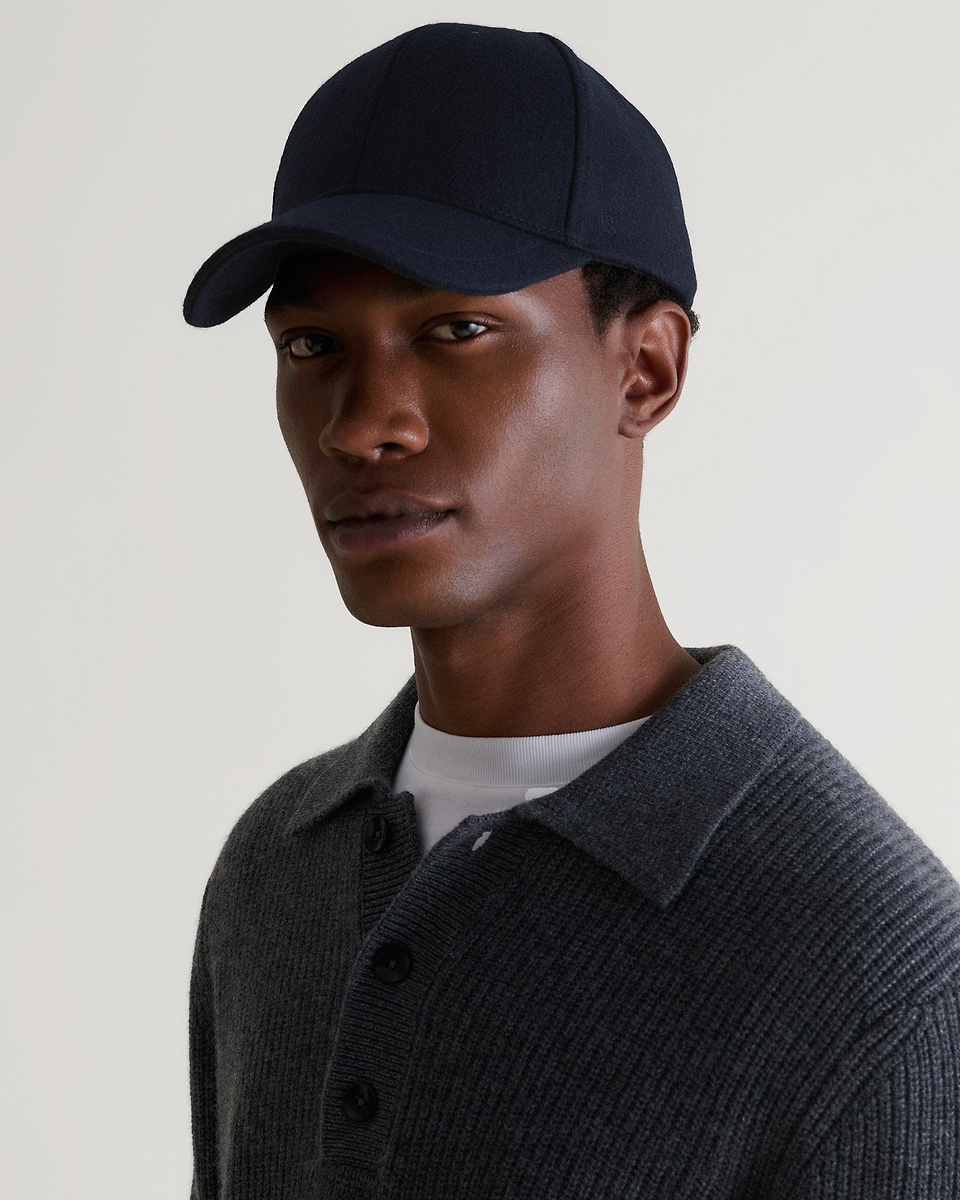 Side view of man wearing navy cashmere merino wool baseball cap with white T-shirt and grey ribbed jumper.