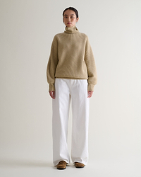 Front view of woman wearing beige cashmere merino Ottoman ribbed roll neck jumper with white jeans and tan suede shoes.