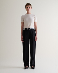 Front view of woman wearing Rise & Fall's cream superfine merino wool knitted t-shirt. Worn with black trousers and belt.